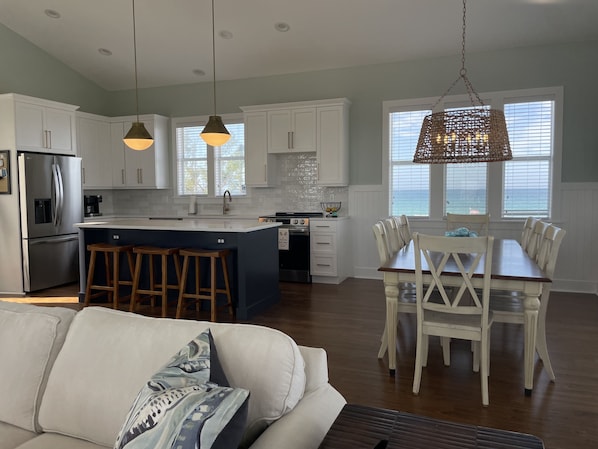 A modern kitchen with white cabinets, a stainless steel refrigerator, and a dining area with a wooden table and white chairs.