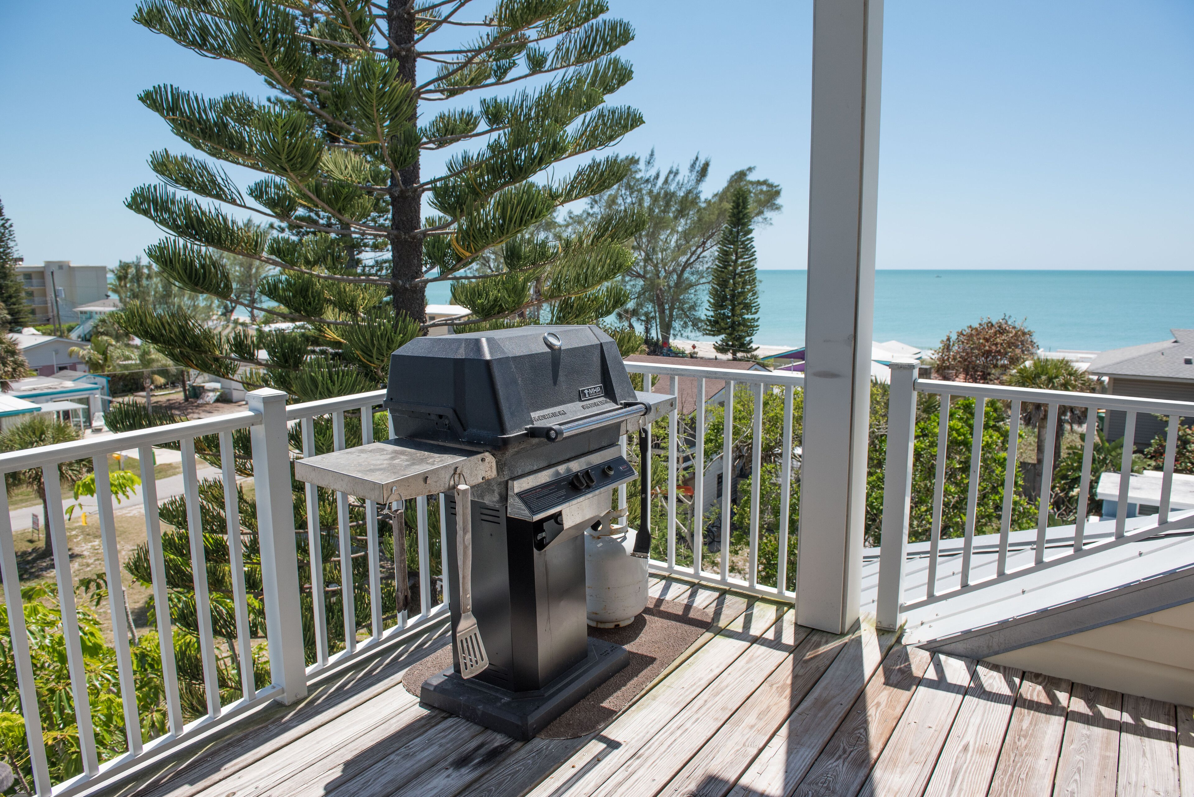 A barbecue grill on a wooden deck with a view of the ocean and a white railing.
