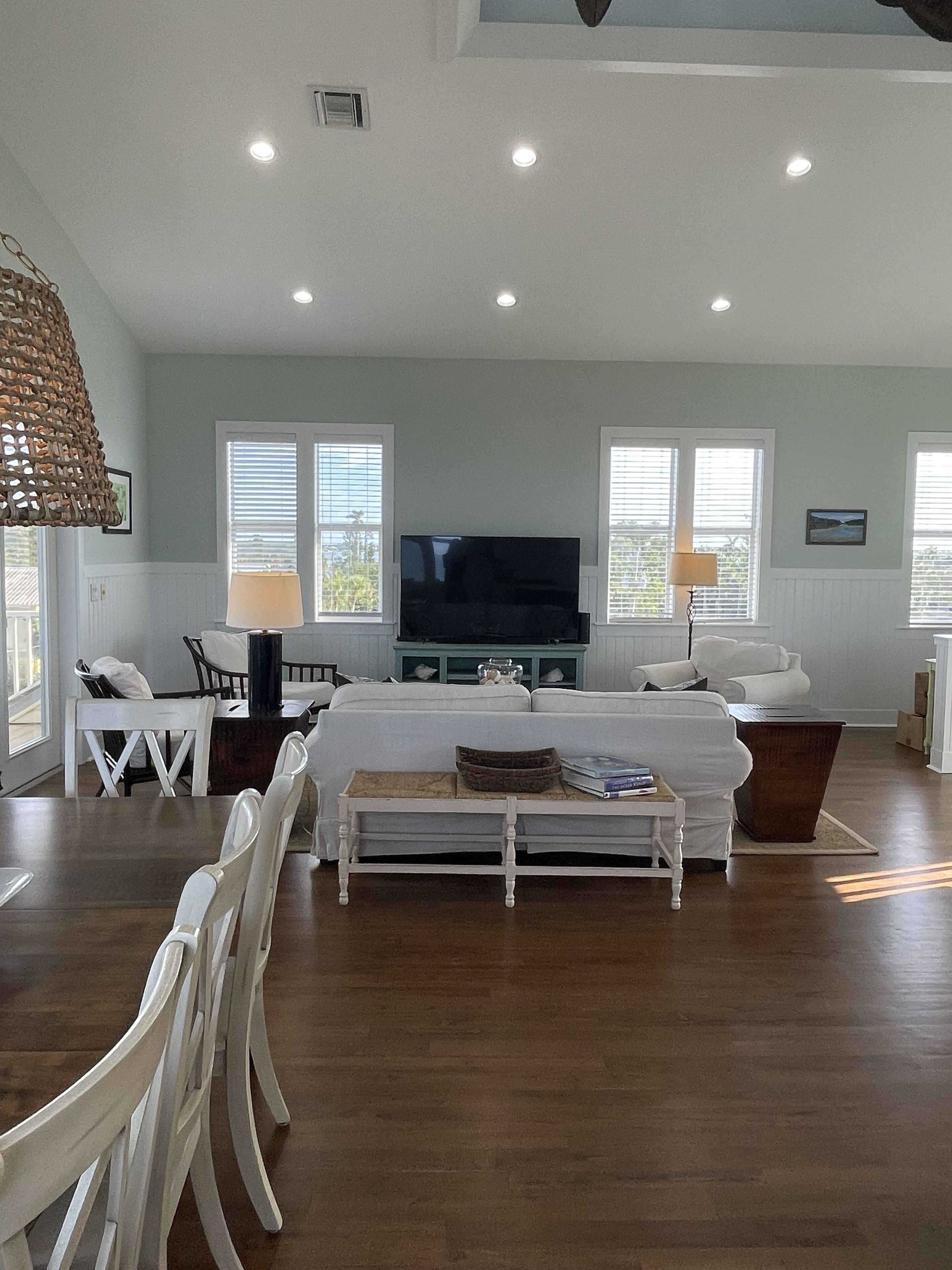 Amplia sala de estar con un televisor de pantalla plana grande, un comedor con sillas blancas y piso de madera.