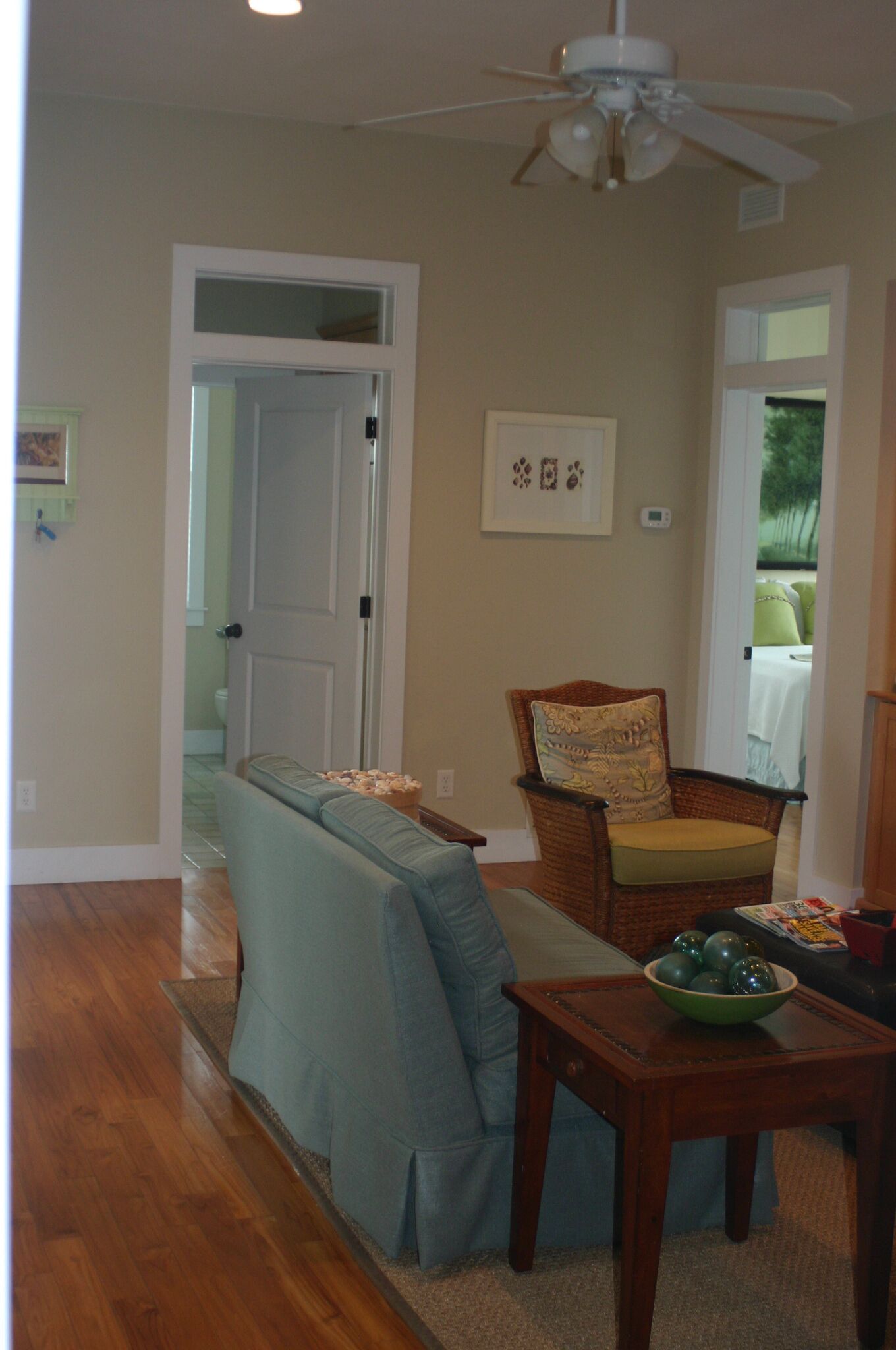 A living room with a wooden floor, a blue sofa, a wicker chair with a cushion, and a small wooden table with a bowl.