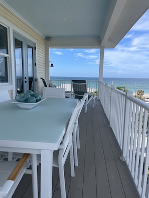 A covered outdoor deck with a table and chairs, overlooking the ocean.