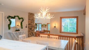 A dining area with a white table and chairs, a stone accent wall, a chandelier, and a window with a view of trees. - Beautiful Mountain Getaway - Last Minute Booking Promos! Minutes from Manchester (Peru)