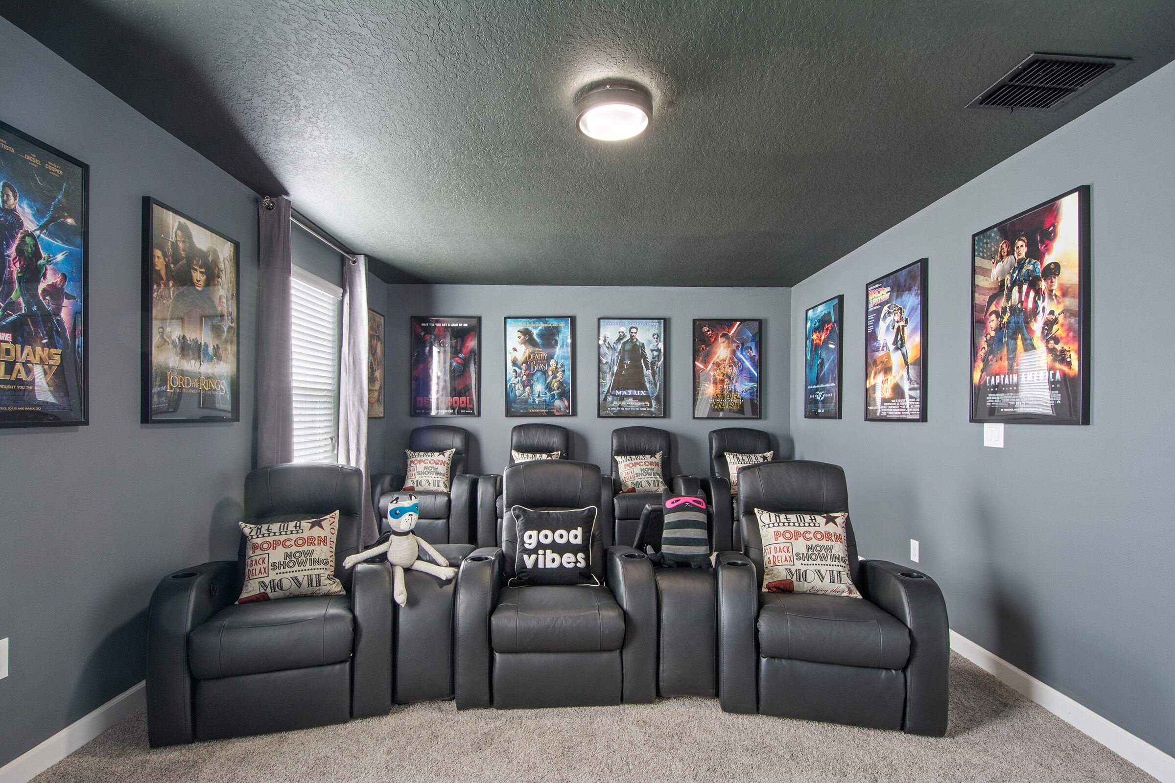Une salle de cinéma privée avec six fauteuils noirs inclinables, une moquette moelleuse et des affiches de films accrochées aux murs.