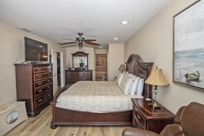 A bedroom with a bed, dresser, TV, ceiling fan, and a painting on the wall. - SeeRay Shores 202 (St. Augustine)