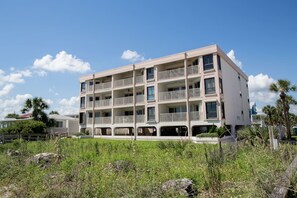 A multi-story building with balconies, located in a grassy area with palm trees. - SeeRay Shores 202 (St. Augustine)
