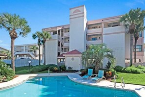 A hotel with a swimming pool, palm trees, and a multi-story building with balconies. - SeeRay Shores 202 (St. Augustine)