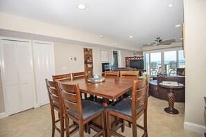 A dining area with a wooden table and chairs, a television, and a view of the ocean. - SeeRay Shores 202 (St. Augustine)