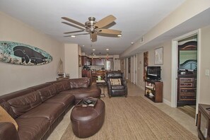 A living room with a sectional sofa, a leather armchair, a TV stand, and a ceiling fan.