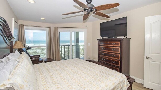 Une chambre d’hôtel avec un lit, un ventilateur de plafond, une télévision, une commode et un balcon donnant sur la plage.