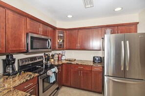 A kitchen with wooden cabinets, stainless steel appliances, granite countertops, and a stainless steel refrigerator. - SeeRay Shores 202 (St. Augustine)