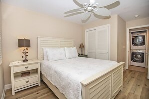 A bedroom with a bed, nightstands, a ceiling fan, a wardrobe, and a washing machine.