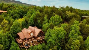 Eine große Holzhütte mit mehreren Balkonen, umgeben von dichtem Wald und Bergen im Hintergrund.