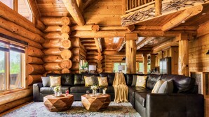 Ein Blockhaushaus-Interieur mit einem großen Ledersofa, zwei Holztischen und einem gemusterten Teppich.