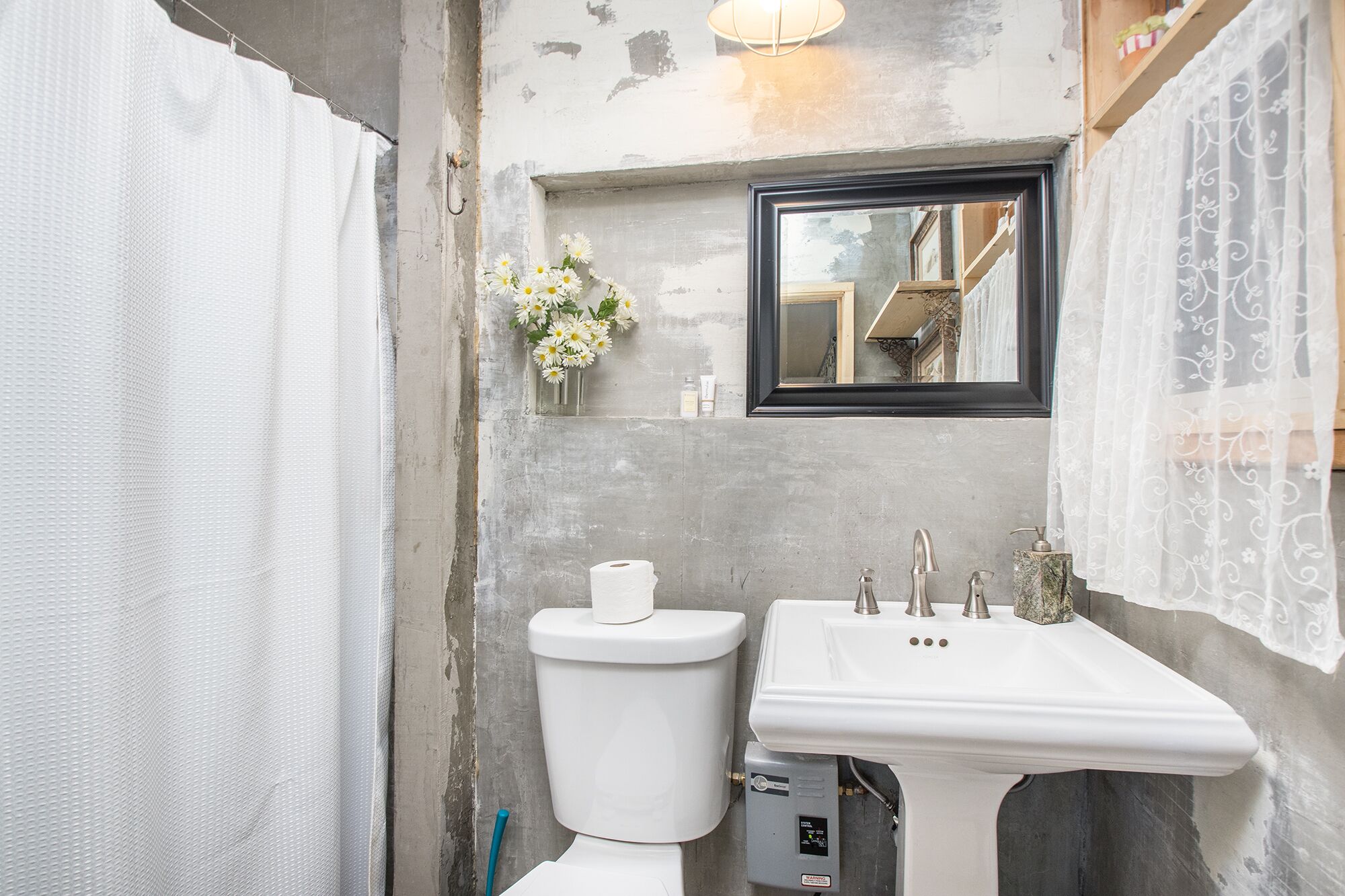 A bathroom with a toilet, sink, and a mirror above the sink. There is a small vase with flowers on the wall.
