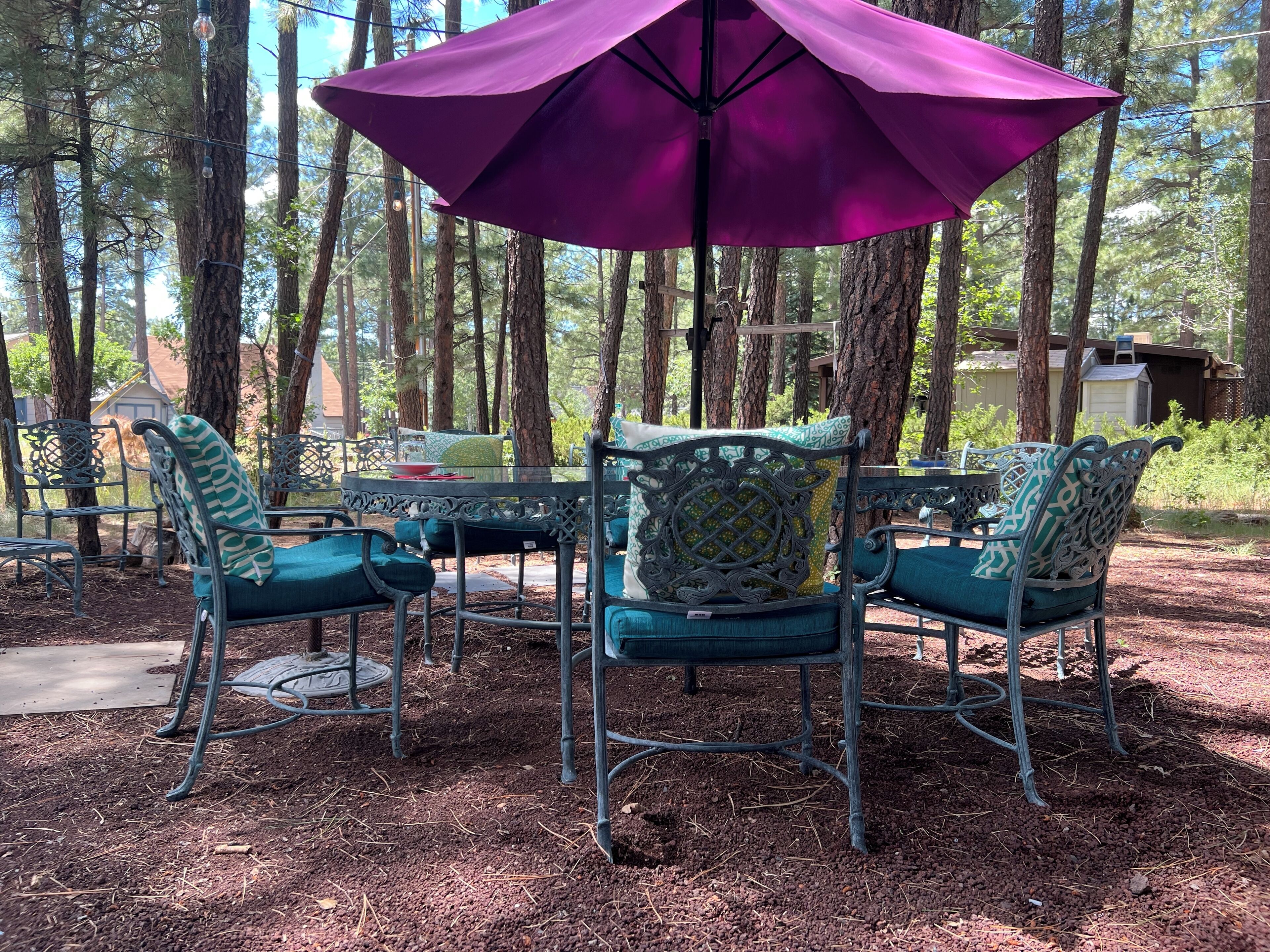 An outdoor seating area with metal chairs and a table, surrounded by trees.