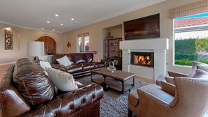 A spacious living room with a fireplace, leather sofas, and a large window offering a view of greenery.