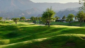 A golf course with rolling green hills, a pond, and a mountain range in the background.