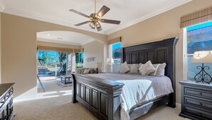 A bedroom with a large bed, a ceiling fan, a dresser, and a view of the outdoors.