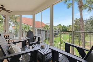 A covered outdoor seating area with a view of a golf course and palm trees.