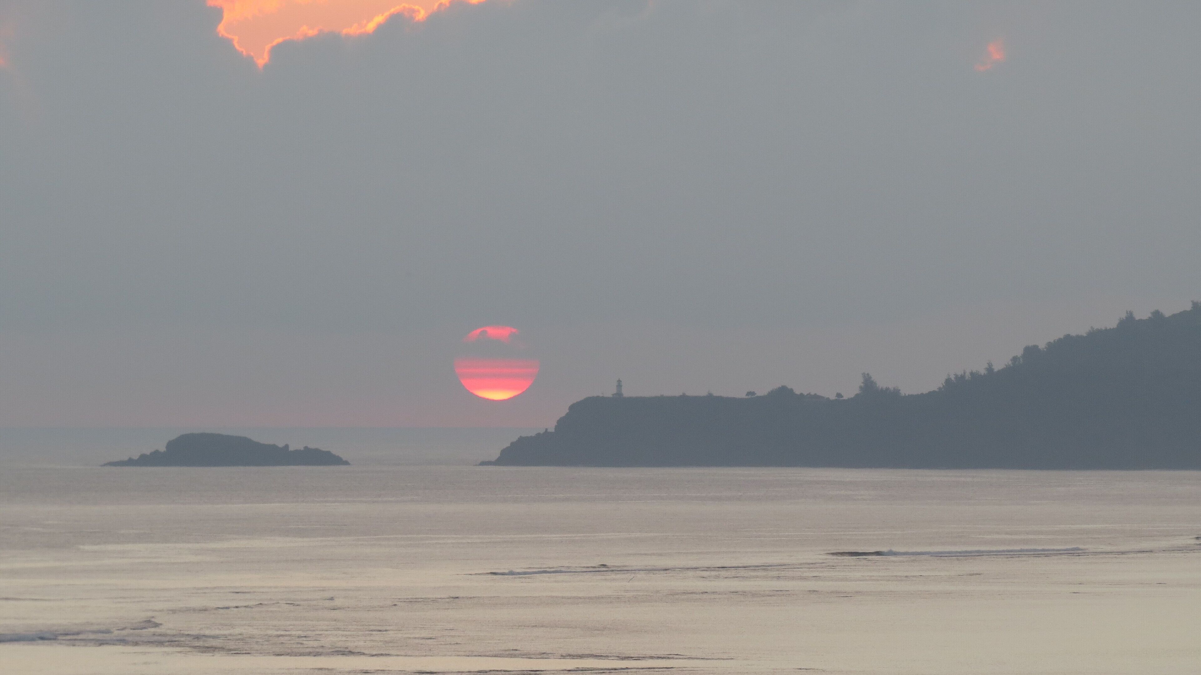 A coastal sunset with a lighthouse on a hill.