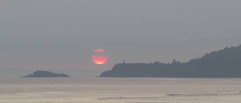 A coastal sunset with a lighthouse on a hill.