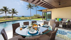 A poolside dining area with wicker furniture, a glass table, and a view of the ocean. - Ocean Views/Private Swimming Pool. Mauna Kea High Bluffs Home (Mauna Kea Beach Resort)