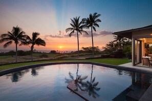Una piscina con vista al atardecer, palmeras y un edificio con puerta de cristal.