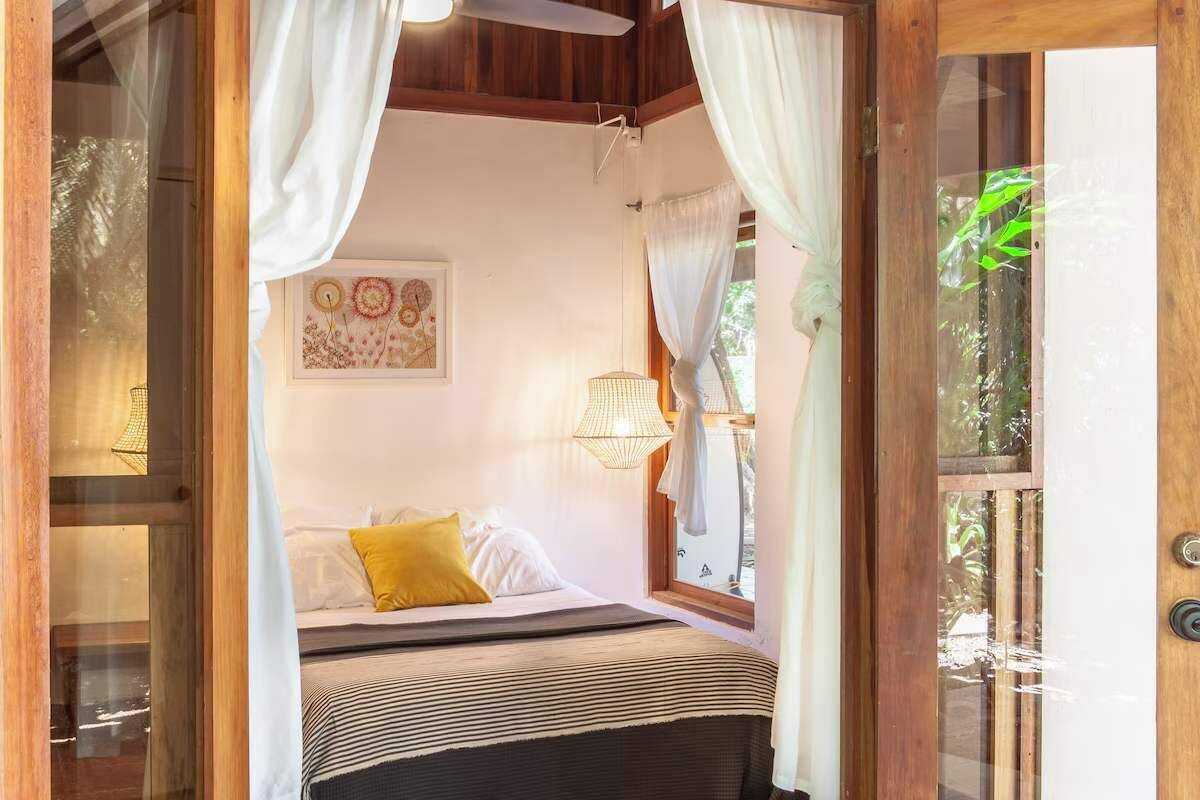 Une chambre à coucher avec un lit, des rideaux, un luminaire suspendu et une fenêtre.