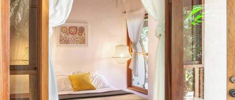 Une chambre à coucher avec un lit, des rideaux, un luminaire suspendu et une fenêtre.