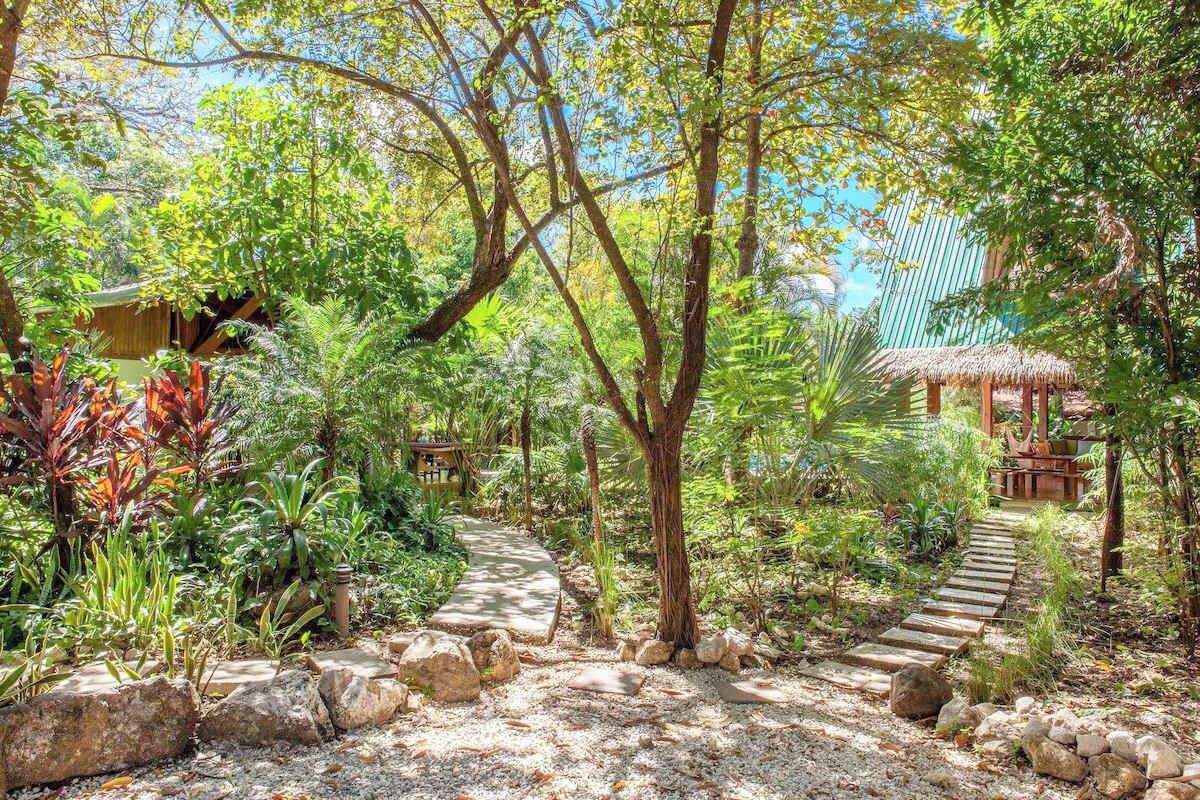 Un sentier de jardin bordé d’une végétation tropicale et agrémenté de structures en bois.