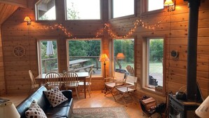 A cozy cabin interior with a wooden interior, a fireplace, a dining area with chairs and a table, and large windows offering views of the outdoors. - ⚓️ Nautical Sea Cabin with Water View ⚓️ (Lopez Island)