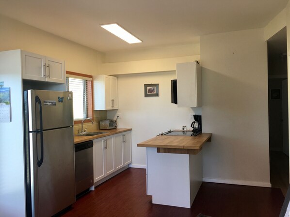 A compact kitchen with white cabinets, a stainless steel refrigerator, a built-in dishwasher, and a wooden countertop. - Fun Suite between two waters (Sechelt)
