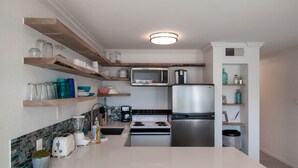 Una cucina moderna con ripiani in marmo bianco, un frigorifero in acciaio inossidabile, un forno a microonde, un piano cottura ed mensole in legno con utensili da cucina.