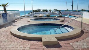 Ein Whirlpoolbereich mit Pool, umgeben von einer Ziegelterrasse und Blick auf einen Strand.
