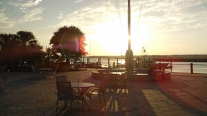An outdoor seating area with tables and chairs, a flagpole, and a view of the water and sunset. - Affordable, Comfortable 2 Bed, 2 Bath Villa - walk to beach! (Kiawah Island)