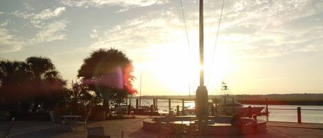 An outdoor seating area with tables and chairs, a flagpole, and a view of the water and sunset.