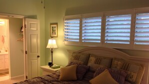 A bedroom with a bed, a nightstand with a lamp, a framed picture, and a window with blinds. - Affordable, Comfortable 2 Bed, 2 Bath Villa - walk to beach! (Kiawah Island)