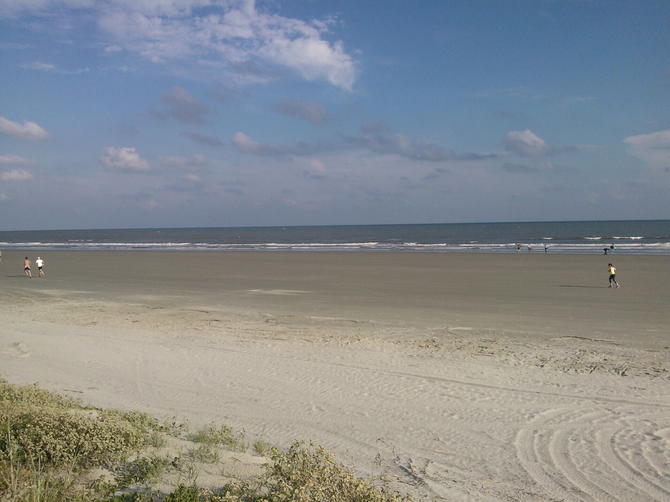 A wide sandy beach with gentle waves and a clear sky.
