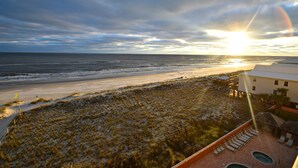 Blick auf einen Strand mit einem Gebäude, einem Pool und einem Sonnenuntergang.