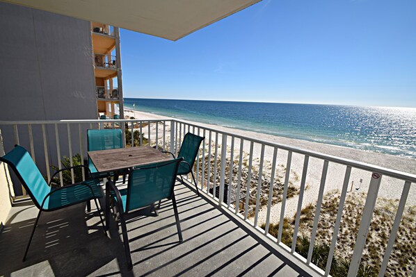 A balcony with a table and chairs, overlooking a beach with a clear view of the ocean.