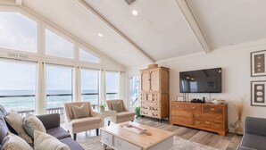 Amplio salón con un gran ventanal con vistas al océano, un televisor y un mueble de madera.