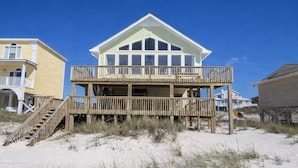 Una casa frente a la playa con una terraza de madera y varios balcones.