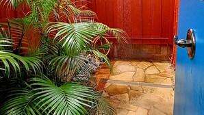 A stone-tiled patio with a red fence and a blue door, under a blue awning. - Slice of Heaven Studio (Waialua)