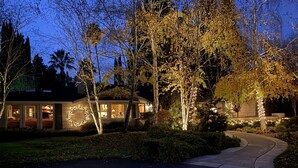 Una casa residencial amb un jardí ben il·luminat, una entrada de cotxes i una decoració de llum circular a la porta principal.