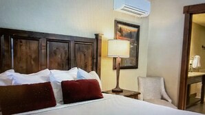 Una habitación de hotel con cama, mesita de noche, lámpara, silla y unidad de aire acondicionado.
