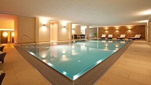 A modern indoor swimming pool with clear water, surrounded by lounge chairs and a stone wall. - Hotel Lipprandt (Wasserburg am Bodensee)
