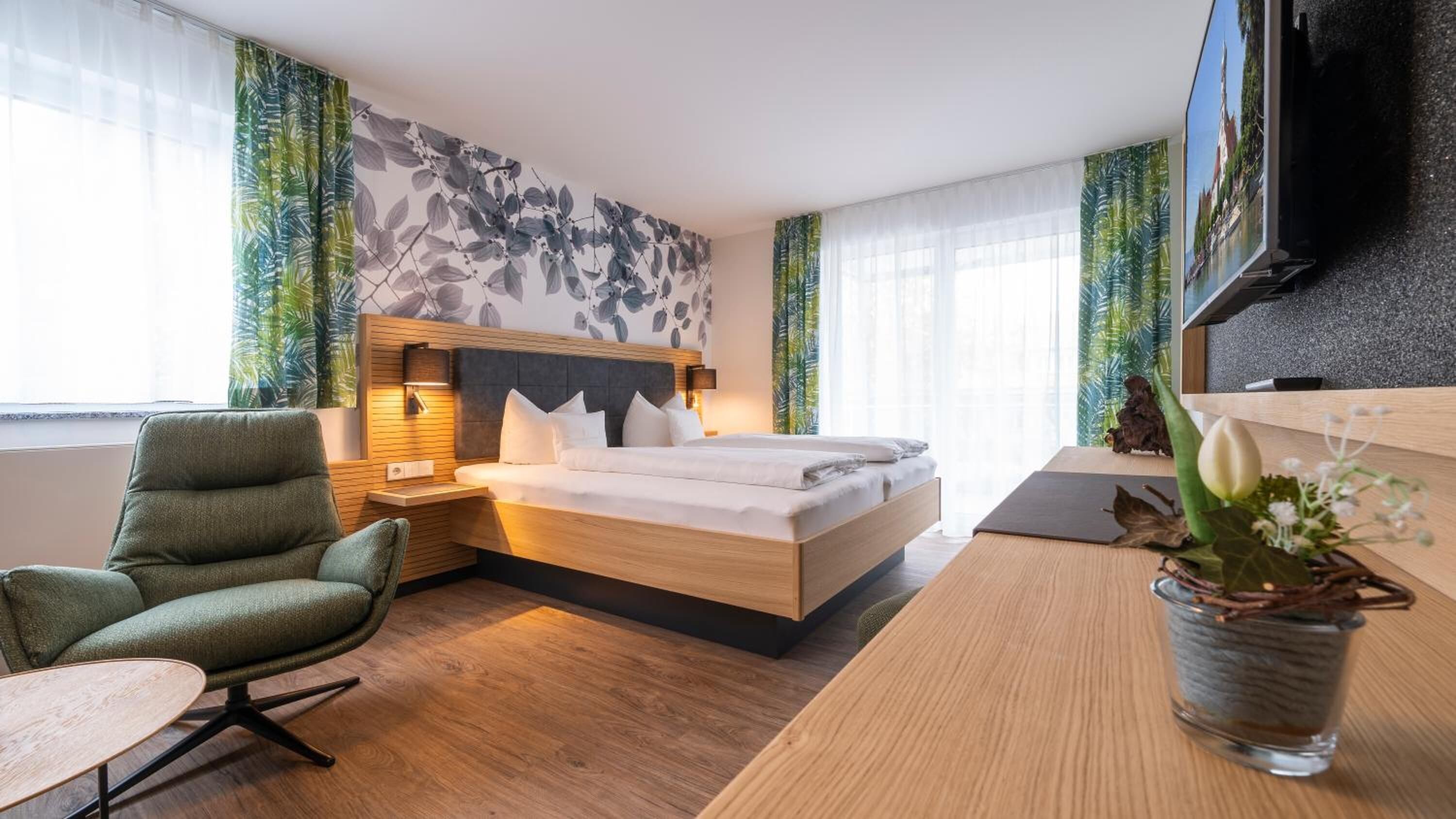 A modern hotel room with a large bed, a desk, a chair, and a TV.