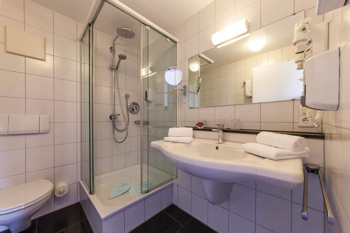 Een moderne badkamer met een douchecabine van glas, een witte wastafel en een toilet.