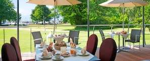 An outdoor dining area with tables set for breakfast, surrounded by chairs, and umbrellas providing shade. - Hotel Lipprandt (Wasserburg am Bodensee)