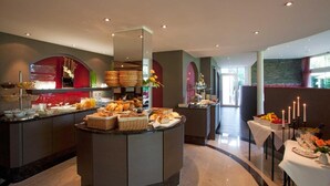 A modern hotel breakfast area with a central buffet, a seating area with a table set for a meal, and a view of the outdoor area. - Hotel Lipprandt (Wasserburg am Bodensee)